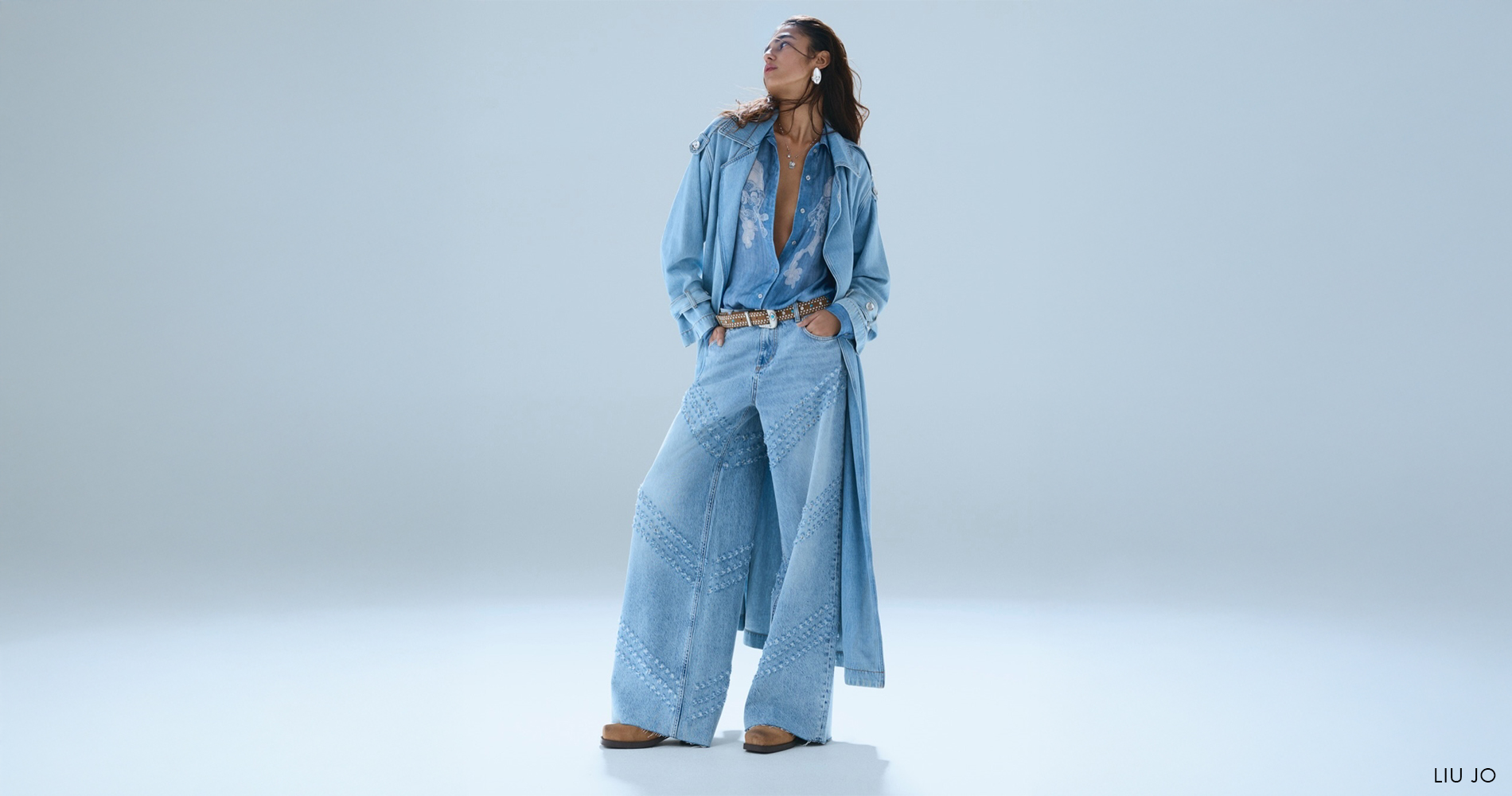 Ženska v total denim videzu s širokimi jeans hlačami, dolgo jeans jakno in denim srajco.